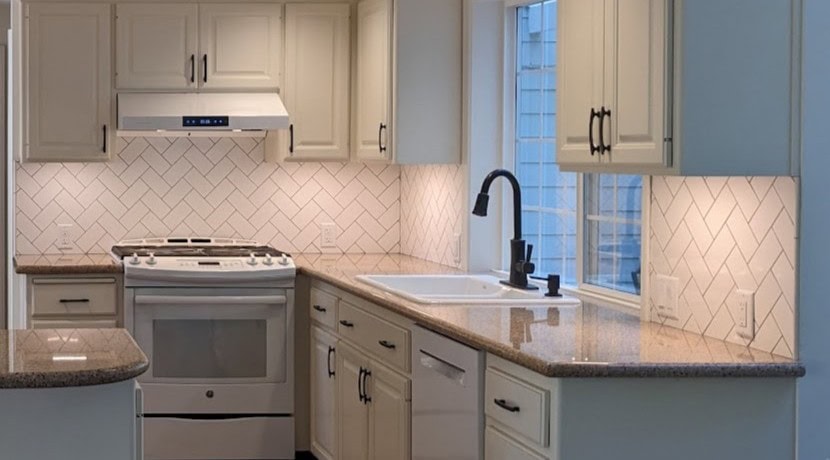 New herringbone tile backsplash installed in a kitchen with cream cabinets and granite counters