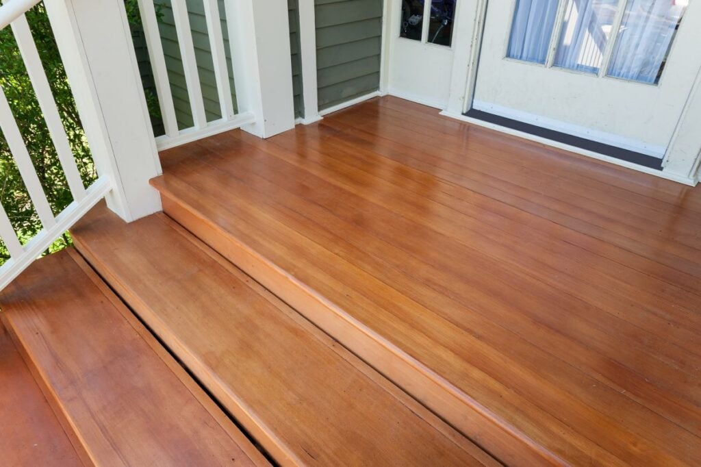 A restored front porch with stained and sealed wood steps and railing painted white