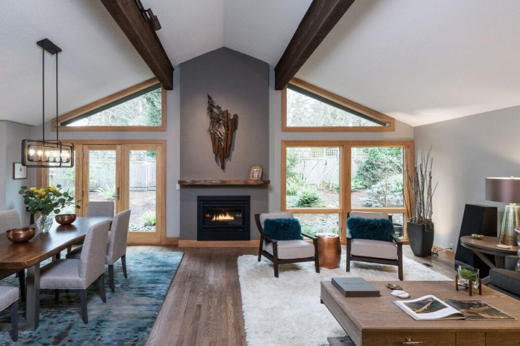 A living room with a vaulted ceiling, a fireplace with a mantel, and floor-to-ceiling windows.