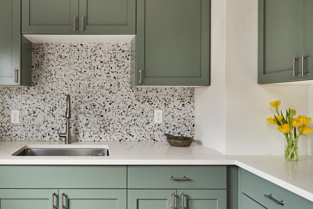 A small kitchen with sage green cabinets, white quartz countertop, and terrazzo tile backsplash