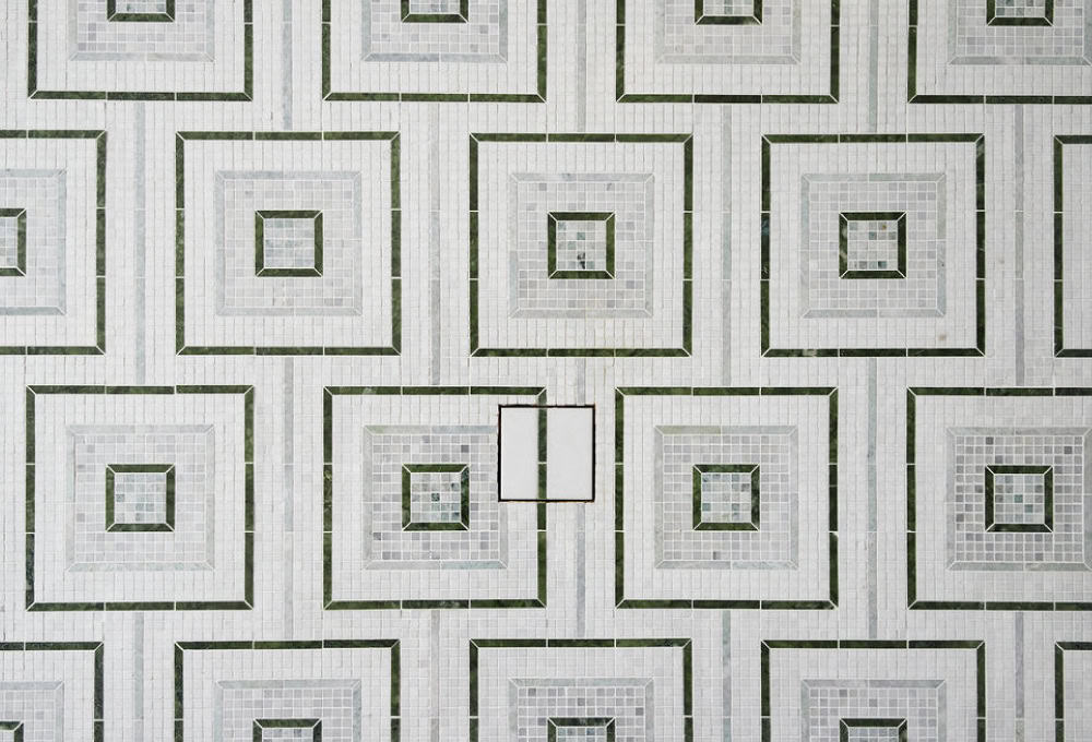Toilet in a transitional bathroom with green tile and mosaic marble floor.