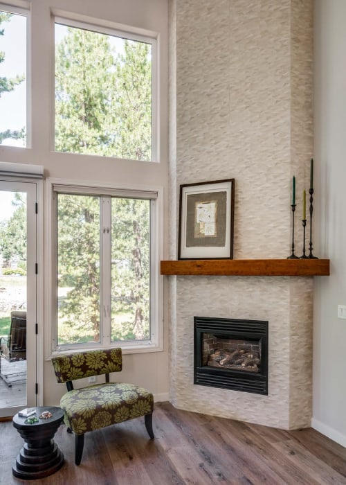 A tall, living room fireplace that is tiled from floor to ceiling with a wooden hearth.