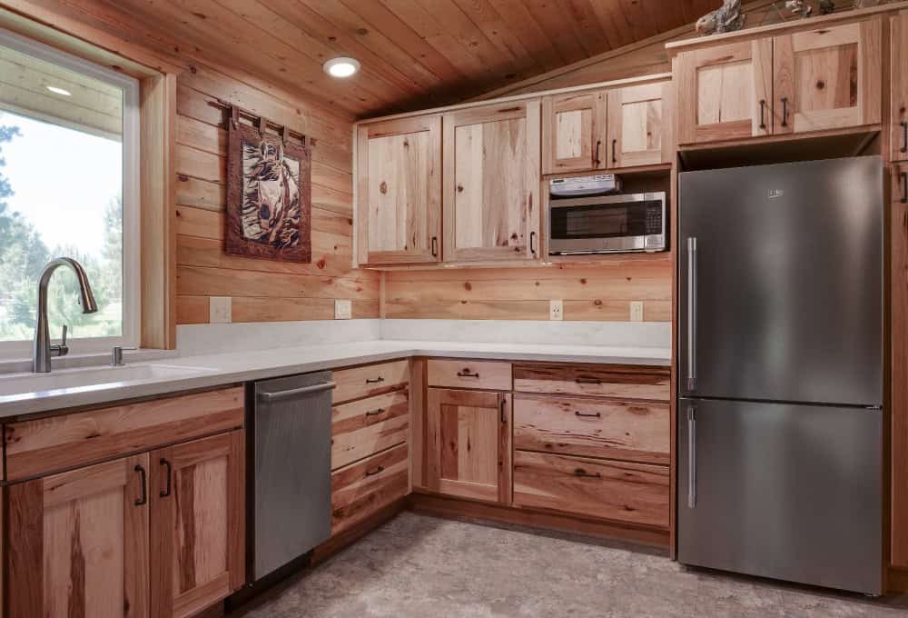 Fully renovated cabin kitchen with stainless steel appliances, a white countertop, and finished wooden cabinets.