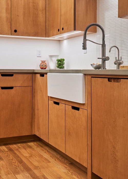 Plywood cabinets and drawers with maple veneer around a porcelain kitchen sink basin.