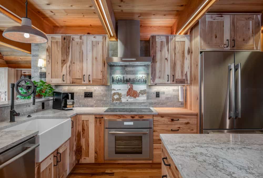 Fully renovated cabin kitchen with stainless steel appliances, a white countertop, and finished wooden cabinets.