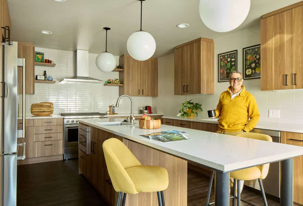 Man in yellow sweater stands in mid-century modern kitchen.