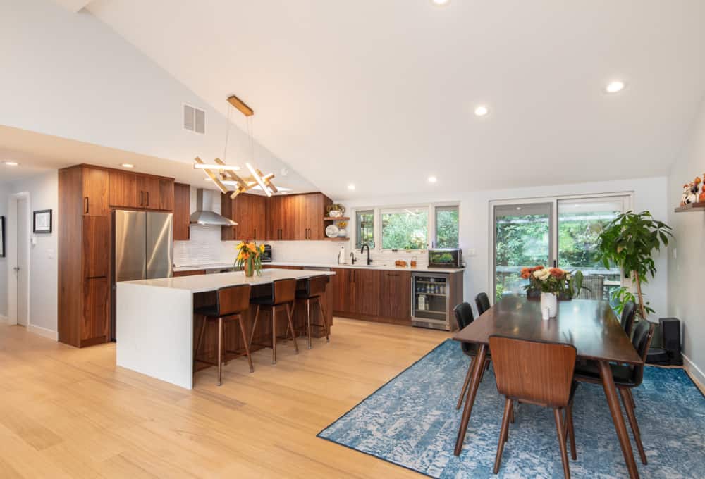 Kitchen with medium-dark wood grain cabinetry, white dimensional backsplash tile, a kitchen island with a waterfall countertop, and matte black fixtures.