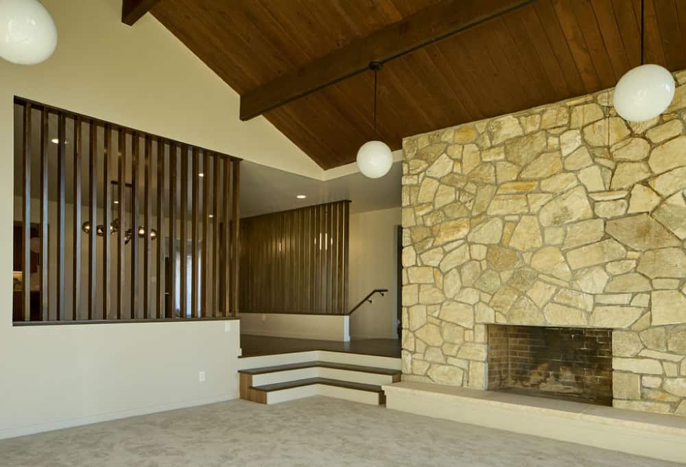 Sunken living room with stone fireplace, wood cathedral ceiling, and carpet.