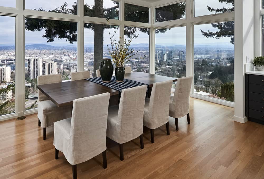 Long wooden kitchen table with eight high-back chairs with grey seat covers.