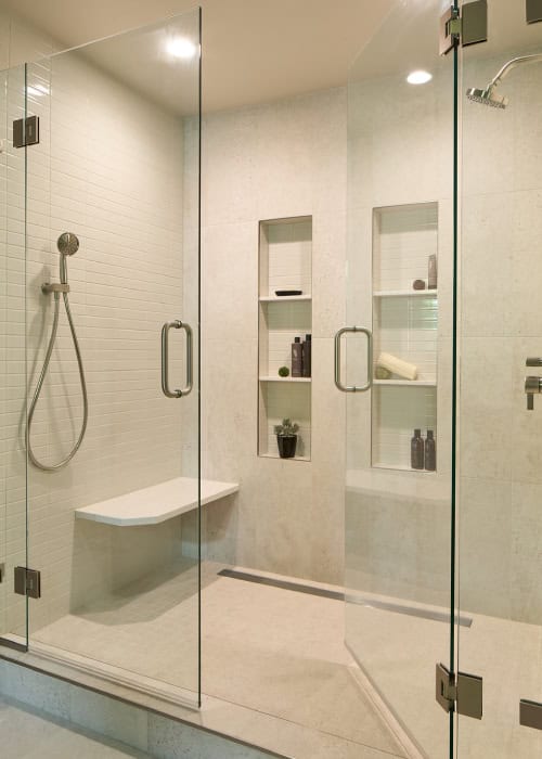 Modern bath with walk-in shower, white tile, and built-in shelving and shower bench with glass doors.