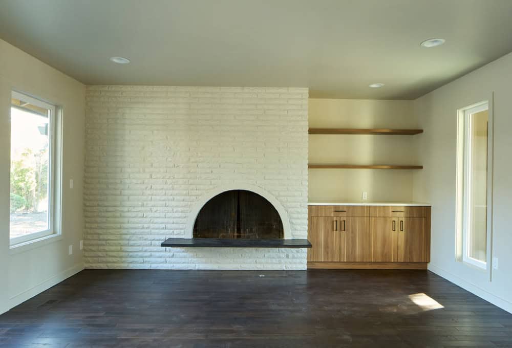 Large room with dark wood floors, white painted brick wall with fireplace, and built-in cabinets with shelving.