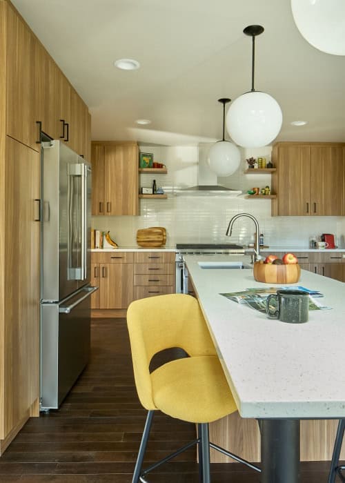 Mid-century style kitchen with pendant lighting, yellow chairs, and built-in cabinets.