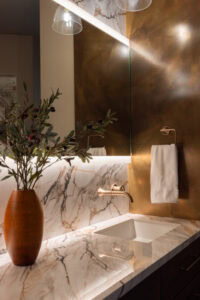 A contemporary primary bathroom vanity with layered lighting and a wall-mounted faucet