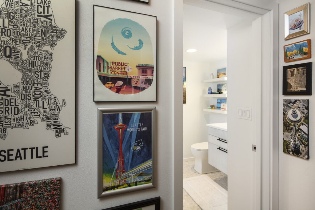 The bathroom seen from the hallway gallery wall of framed Seattle prints and neighborhood maps.