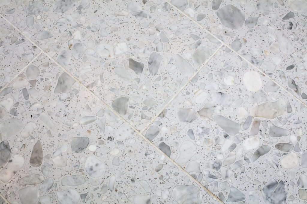 White terrazzo floor tile with large marble aggregate, laid on a diagonal.