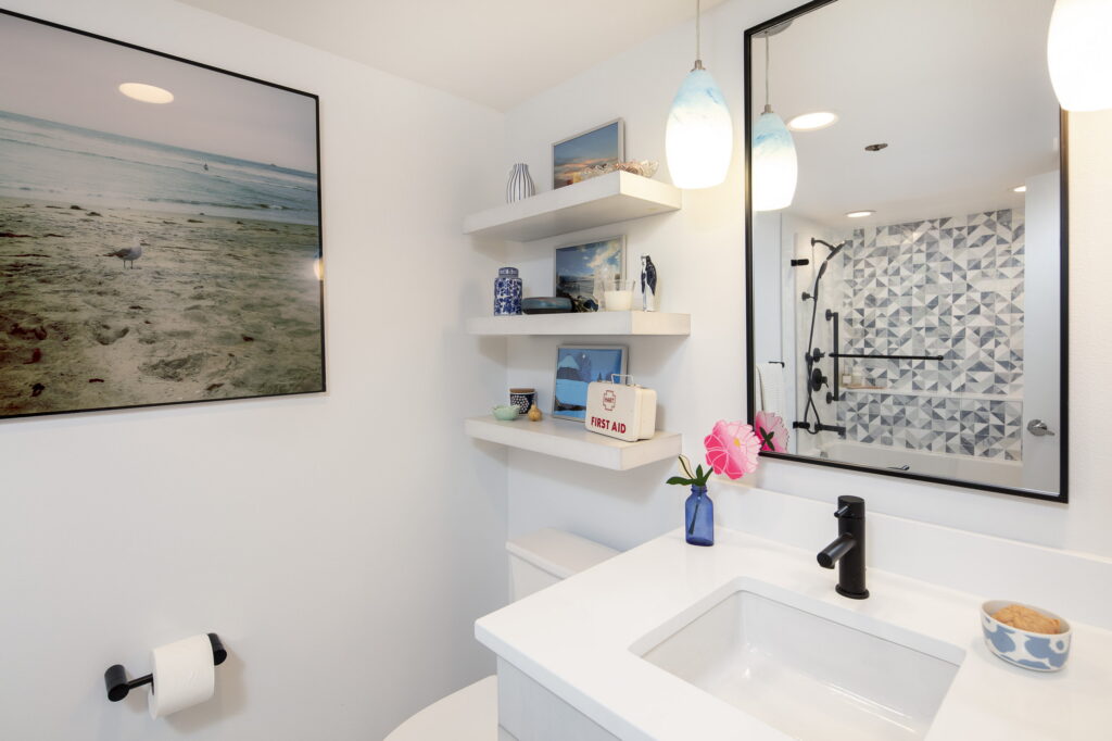 Vanity with a black-framed mirror and blue art-glass pendants, the tiled tub reflected in the glass.