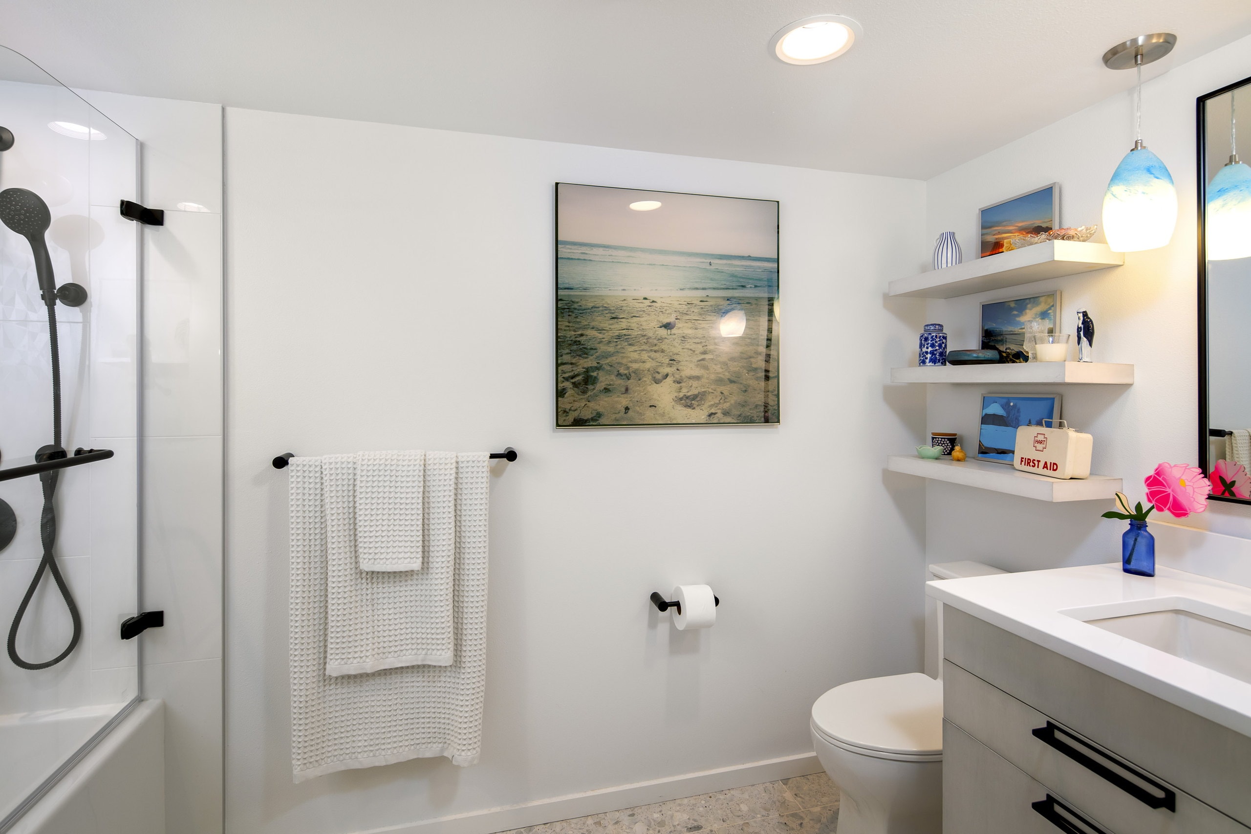 Remodeled Belltown condo bathroom with a glass-panel tub shower at left, floating shelves, and a white quartz vanity at right.