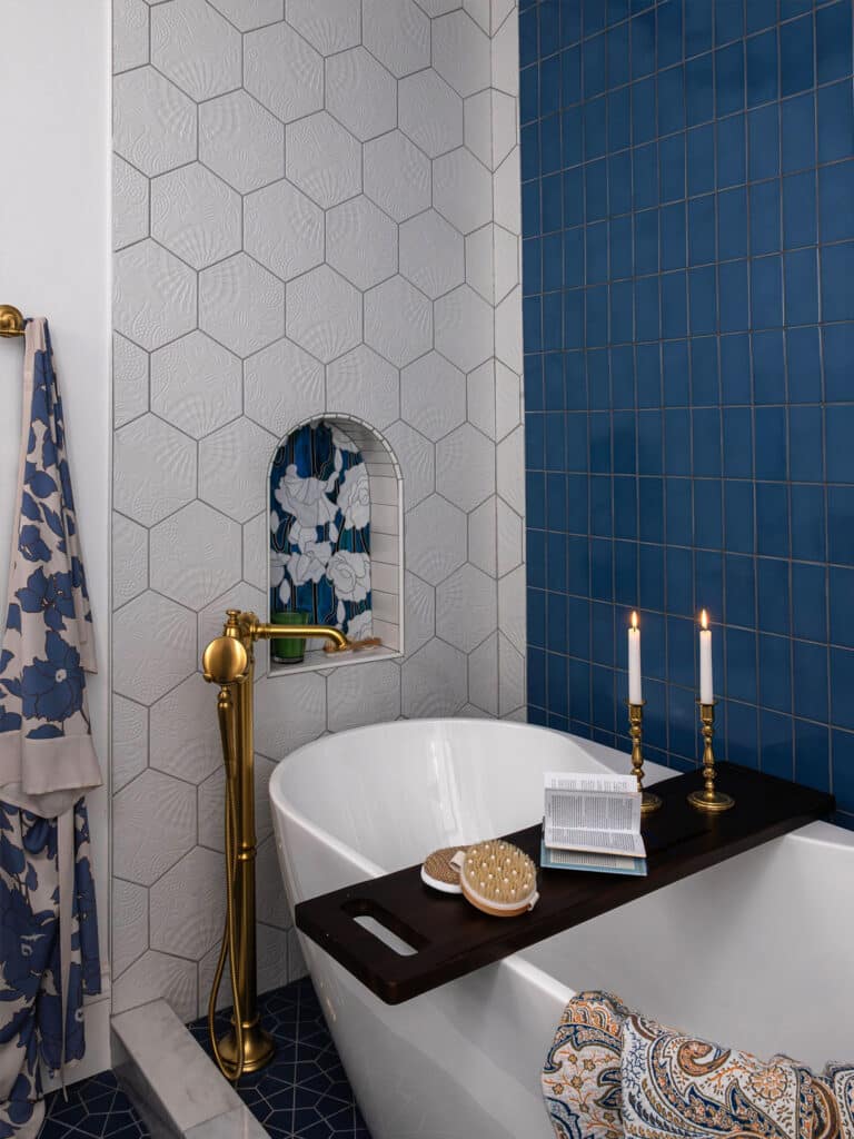 Bathroom remodel featuring a navy blue tile accent wall, hexagon tile, and freestanding tub with brass fixtures.