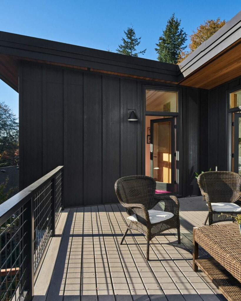 Dark board-and-batten siding meeting the cedar soffit above the deck, with a black-framed glass door.