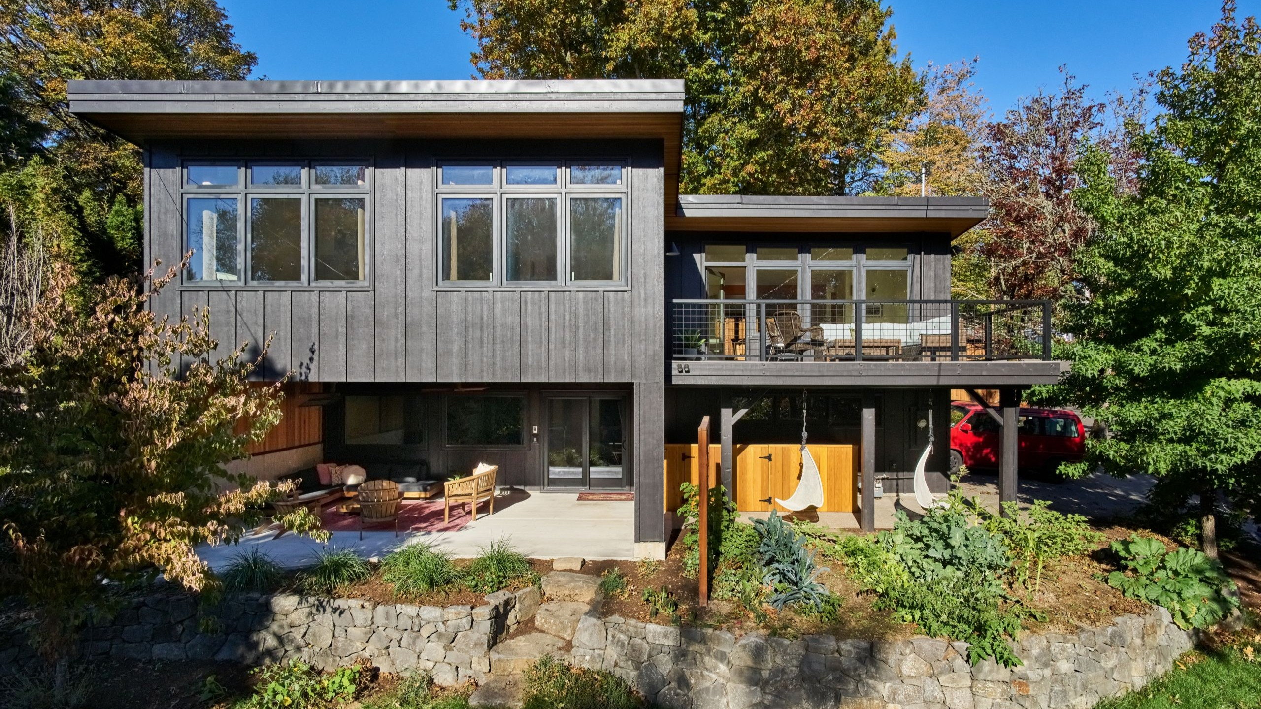 Rear elevation of the remodeled Council Crest home, with dark board-and-batten siding, cedar soffits, and a cantilevered deck.