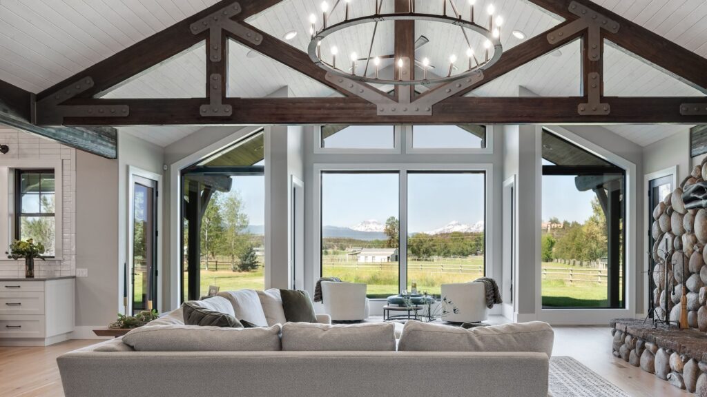 The living room of a remodeled Tumalo family lodge with exposed trusses, a grey sectional sofa, and a view of the property