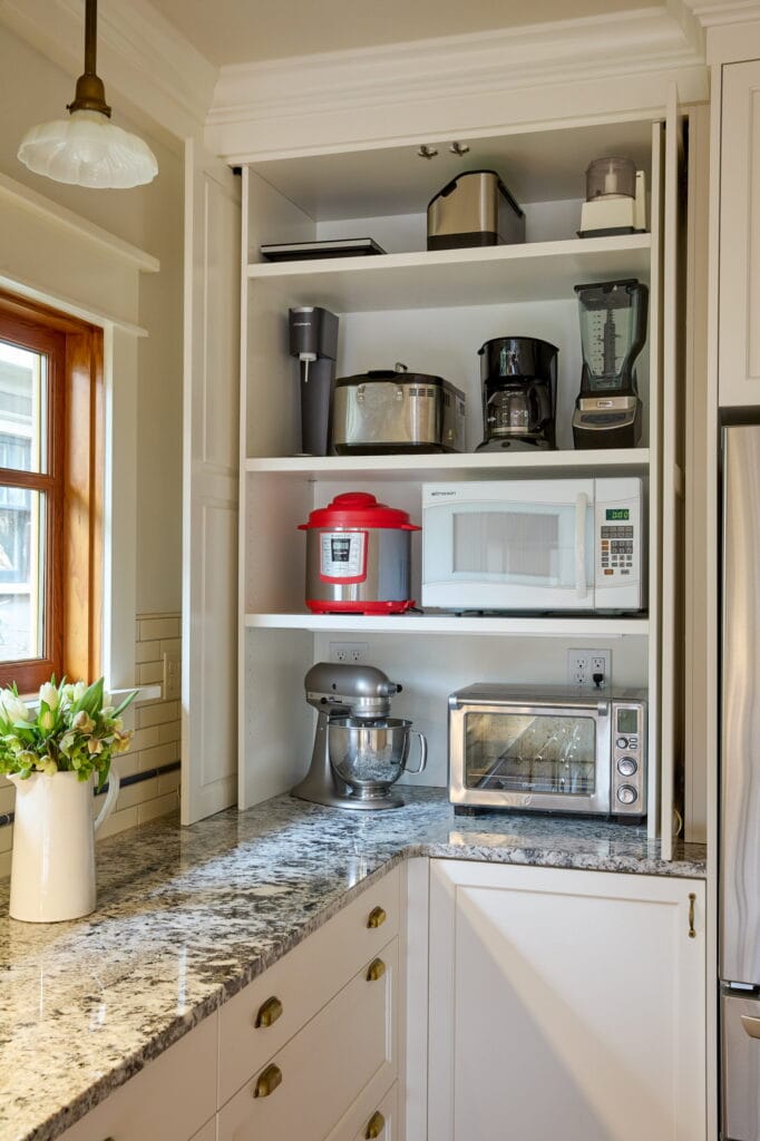 Appliance garage with bi-fold doors open, holding a microwave, mixer, blender, and coffee maker on adjustable shelves.