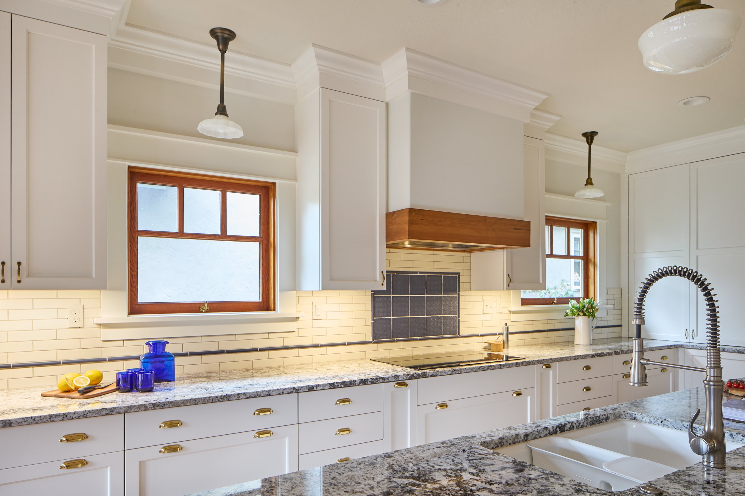 The cooktop wall beneath a fir-wrapped hood, flanked by fir-trimmed windows and a subway tile backsplash.
