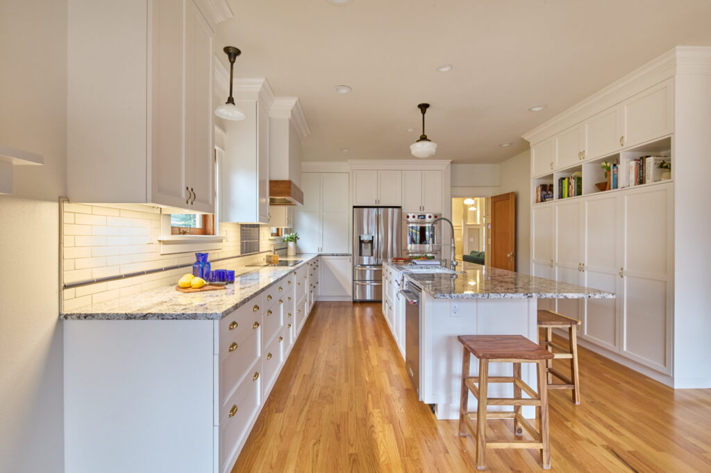 The length of the kitchen, with the perimeter run at left, the island at right, and a built-in bookcase wall beyond.