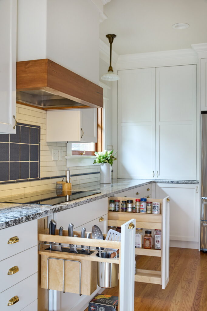 Two narrow pull-outs beside the cooktop, one holding knives and utensils, the other tiered spice racks.