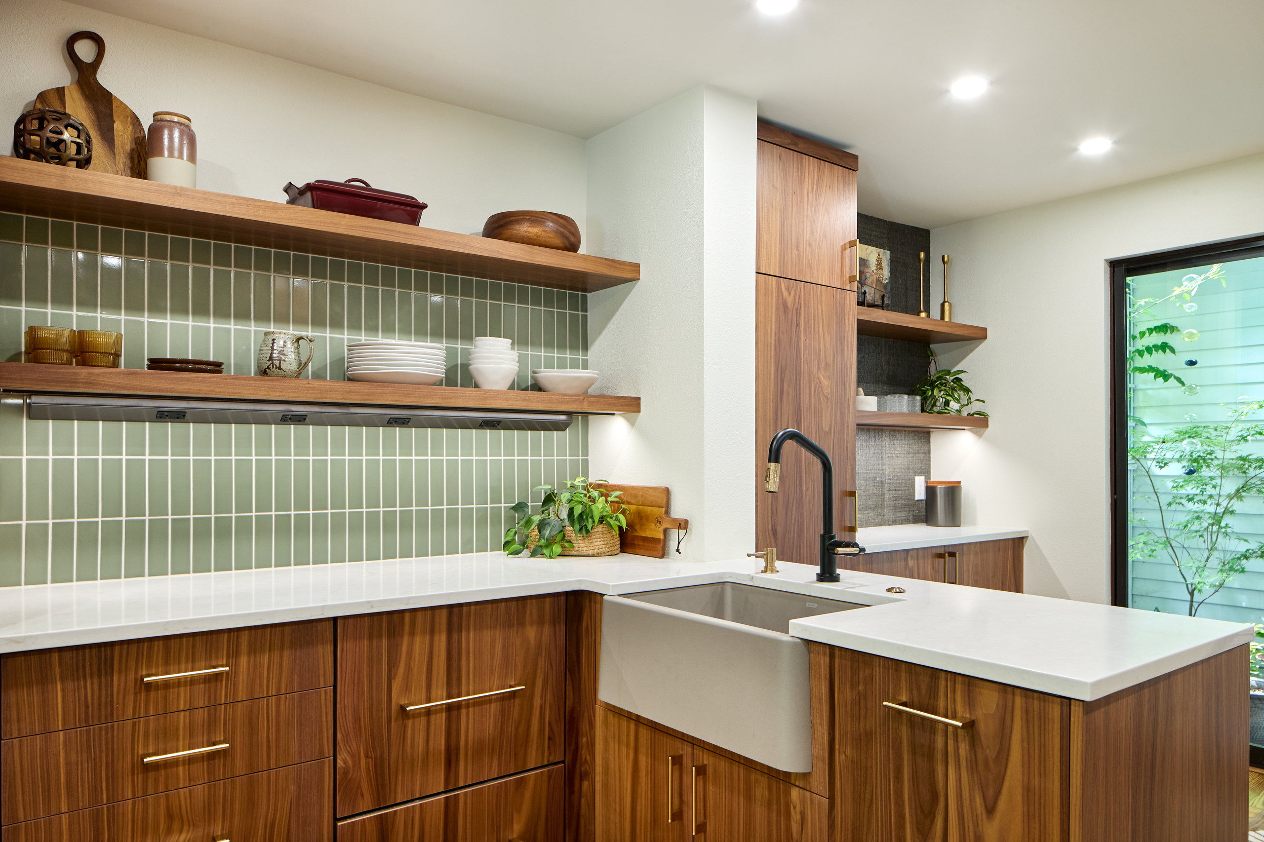 Sink run with a concrete apron-front sink, black-and-brass faucet, and two walnut floating shelves.