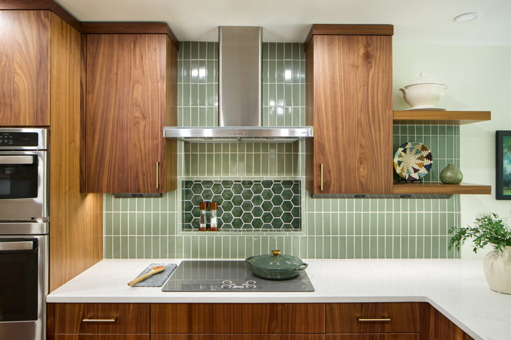 Cooktop wall with a stainless chimney hood and a recessed niche of green hexagonal sunburst tile.