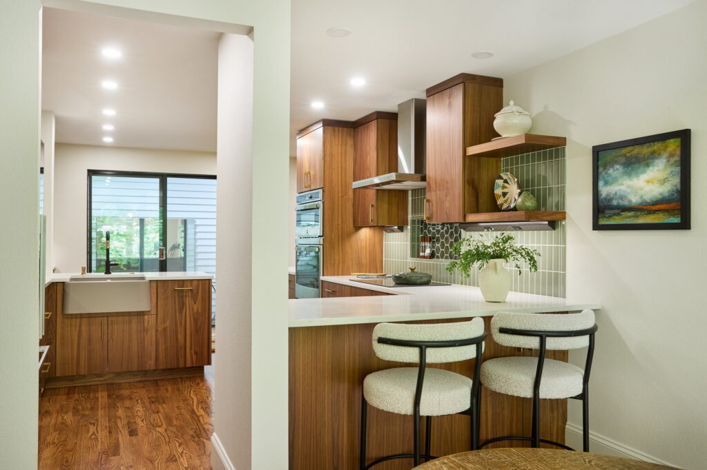 The kitchen from the dining room, with upholstered stools at the quartz peninsula and the cooktop wall beyond.