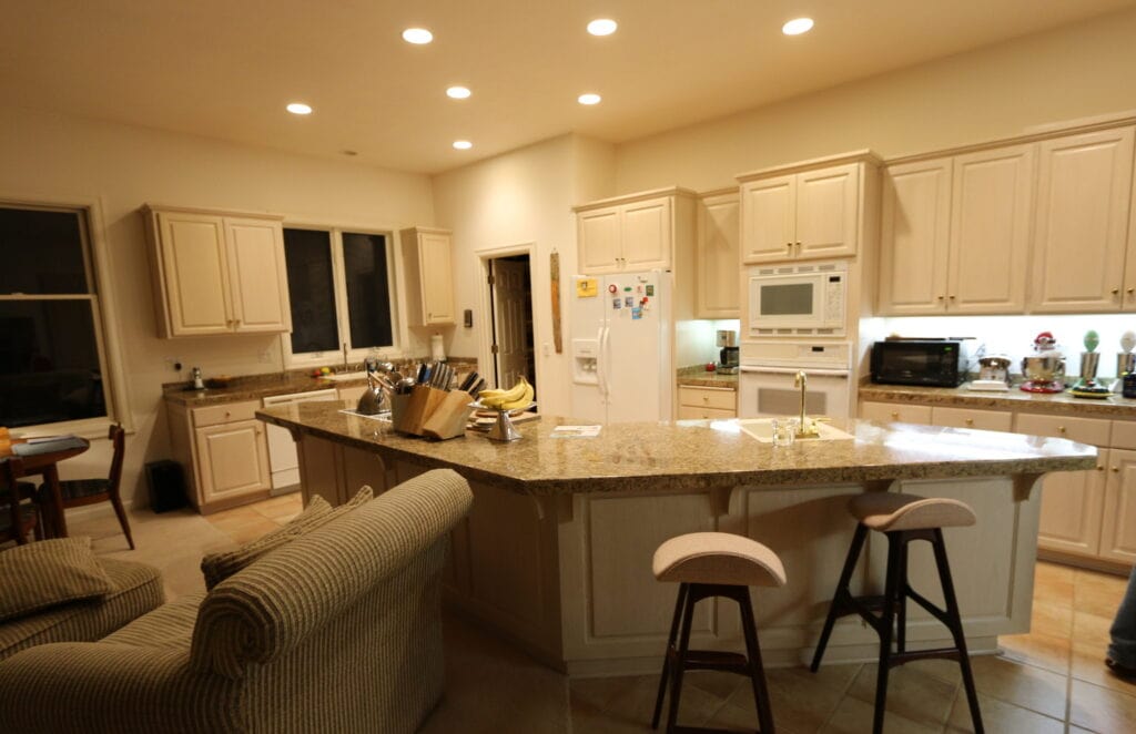 The kitchen before remodeling, with cream raised-panel cabinets, speckled granite counters, white appliances, and tile floors.