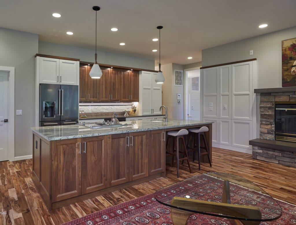 Remodeled McKenzie River kitchen with a walnut island, painted perimeter cabinetry, and a granite-slab backsplash, open to the stone fireplace beyond.