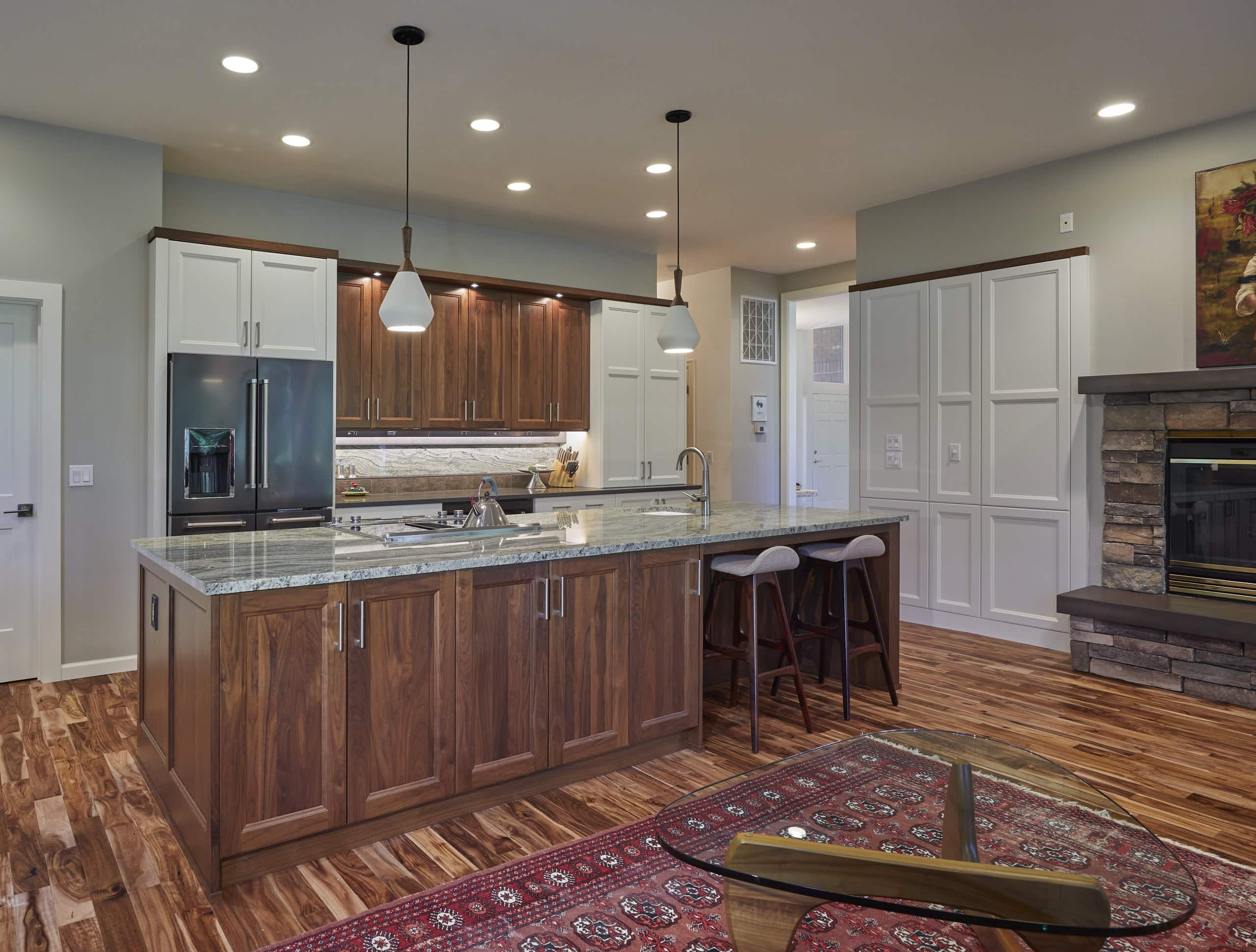 Remodeled McKenzie River kitchen with a walnut island, painted perimeter cabinetry, and a granite-slab backsplash, open to the stone fireplace beyond.
