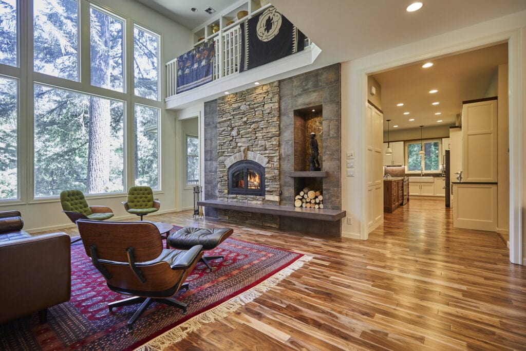 The adjoining living room, with a stacked-stone fireplace rising to the vaulted ceiling beside a two-story window wall.
