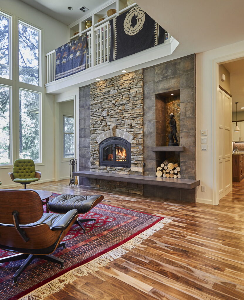 The adjoining living room, with a stacked-stone fireplace rising to the vaulted ceiling beside a two-story window wall.