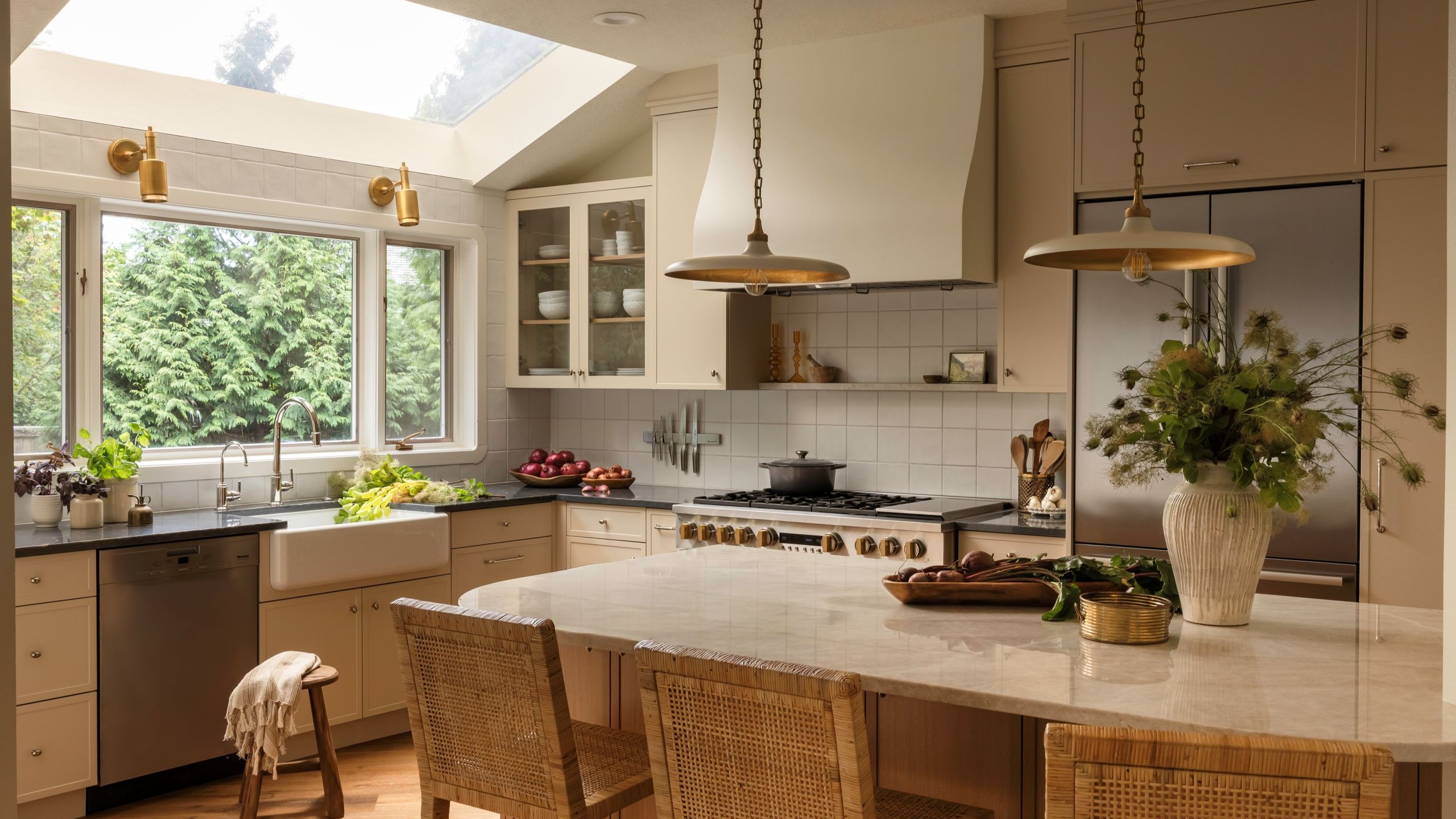 A remodeled kitchen featuring custom warm beige cabinetry, mixed metals, and natural light pouring in from a skylight.