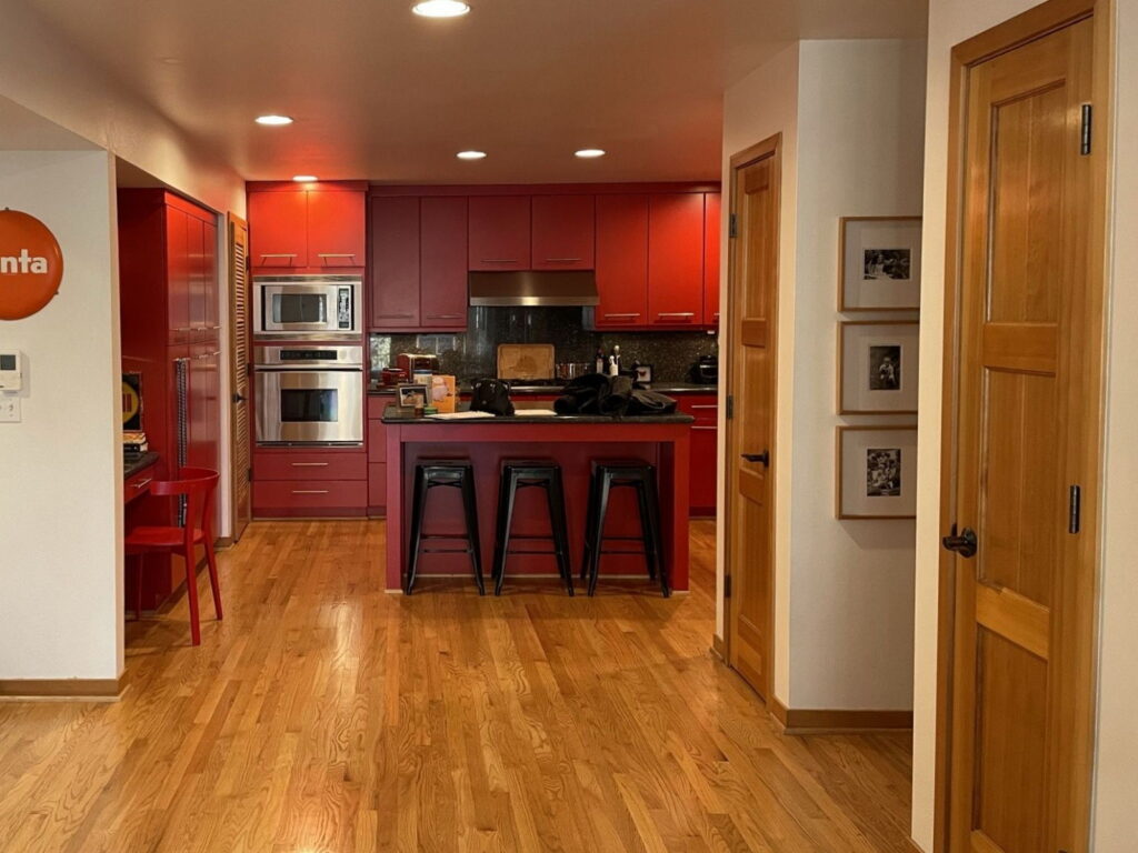 The kitchen before remodeling, with dark red painted cabinetry, black granite counters, and a raised island bar.
