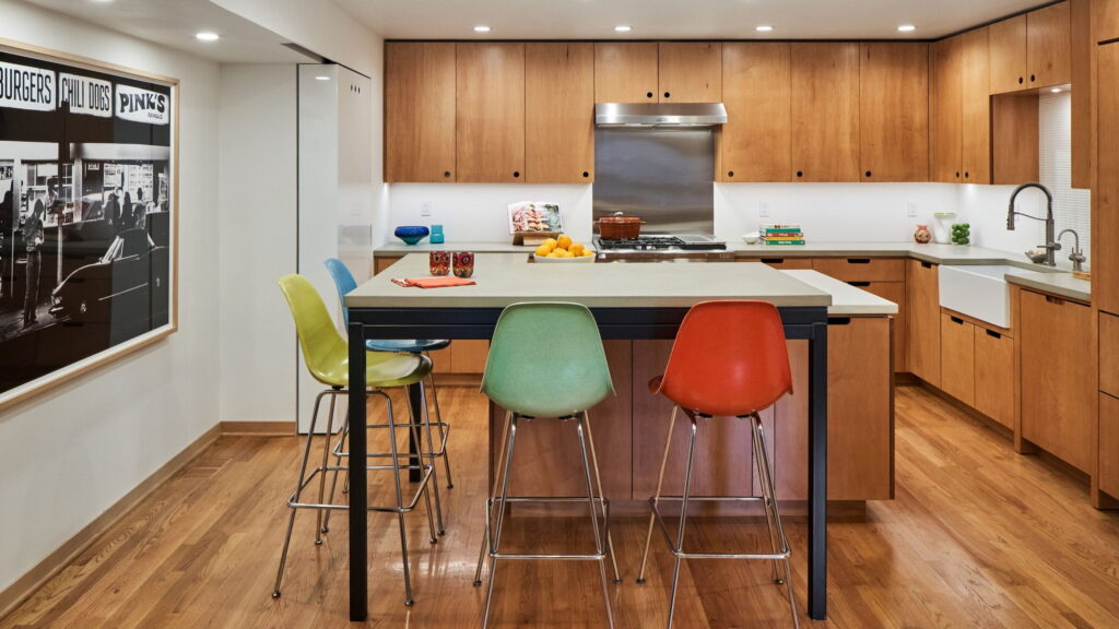 Kitchen island with an integrated steel-framed table and vintage fiberglass stools in yellow, blue, green, and orange.