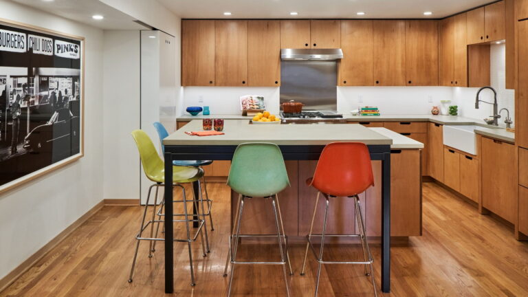 Kitchen island with an integrated steel-framed table and vintage fiberglass stools in yellow, blue, green, and orange.