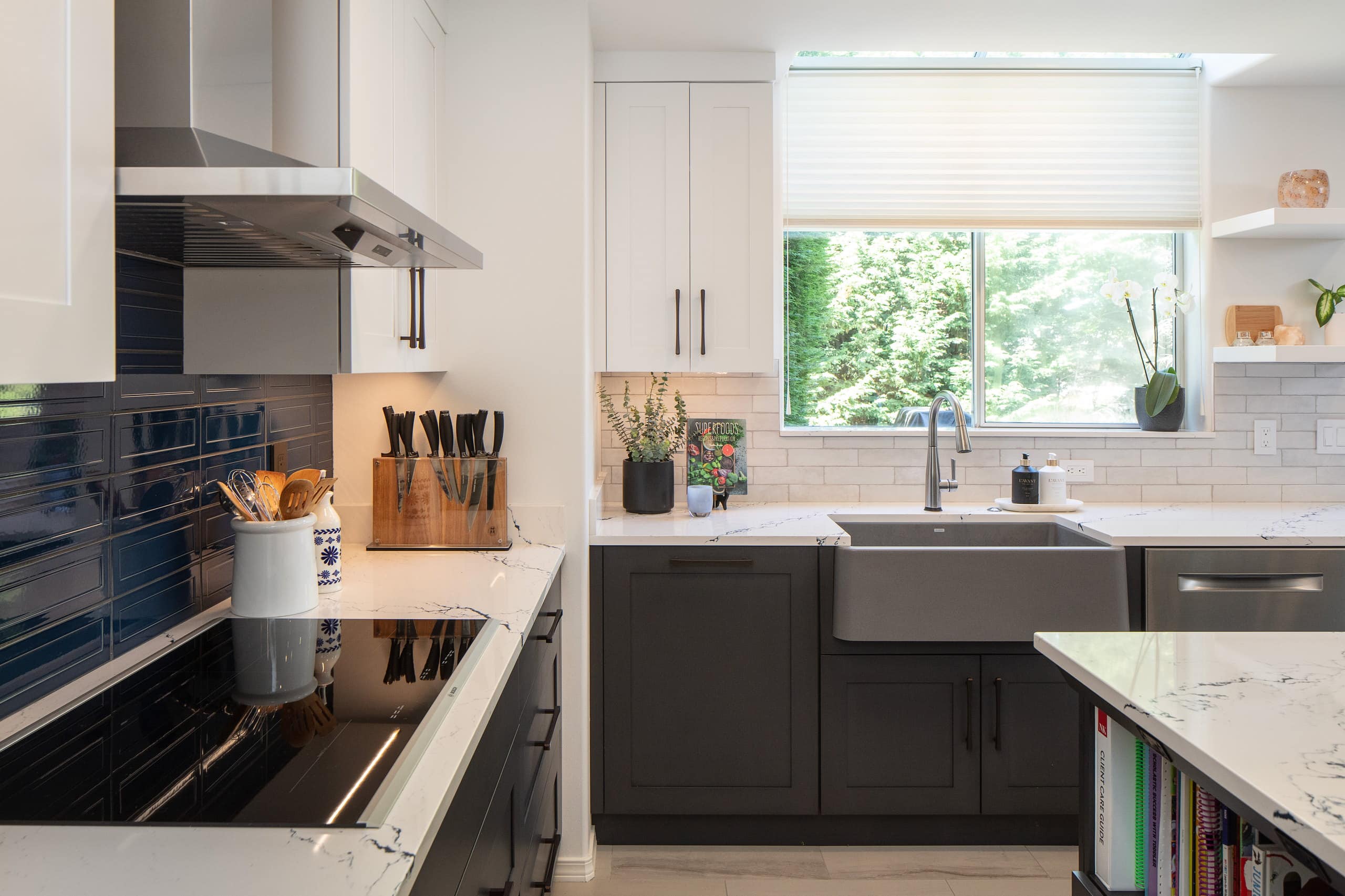 Working run of the kitchen with an induction cooktop under a stainless chimney hood and a farmhouse sink at the window.