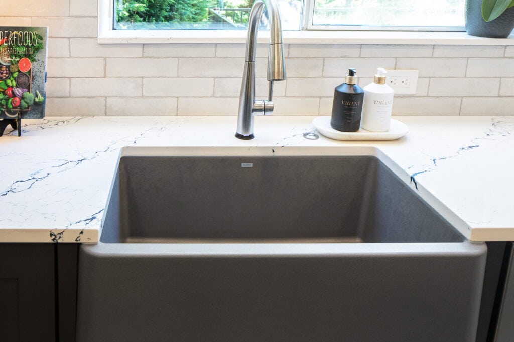 Gray composite farmhouse apron sink set into white quartz with dramatic gray veining.