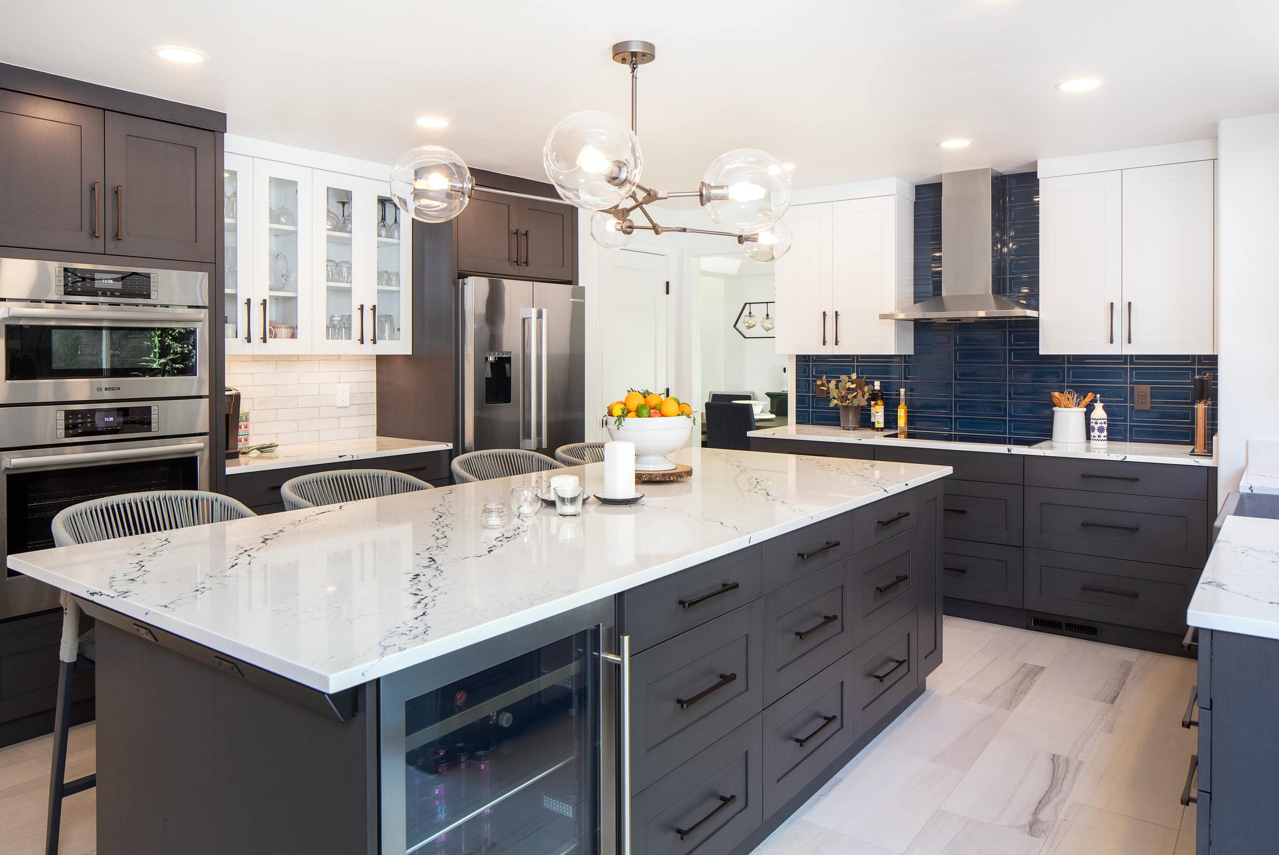 Kitchen island seating beneath a globe chandelier, with stainless double wall ovens and glass-front upper cabinets beyond.