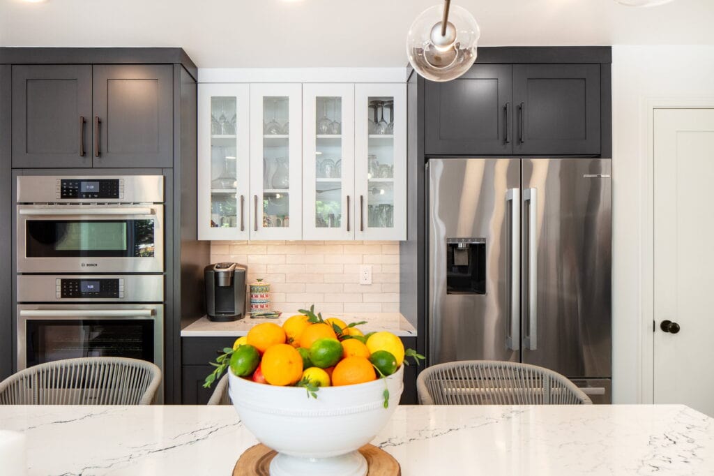 Stainless double wall ovens beside glass-front upper cabinets and a paneled coffee station.