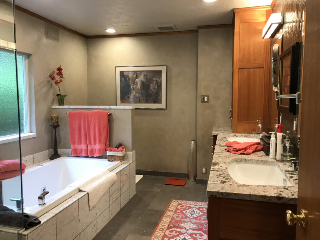 The primary bathroom before remodeling, with a tiled drop-in tub, taupe walls, and dark slate floor tile.