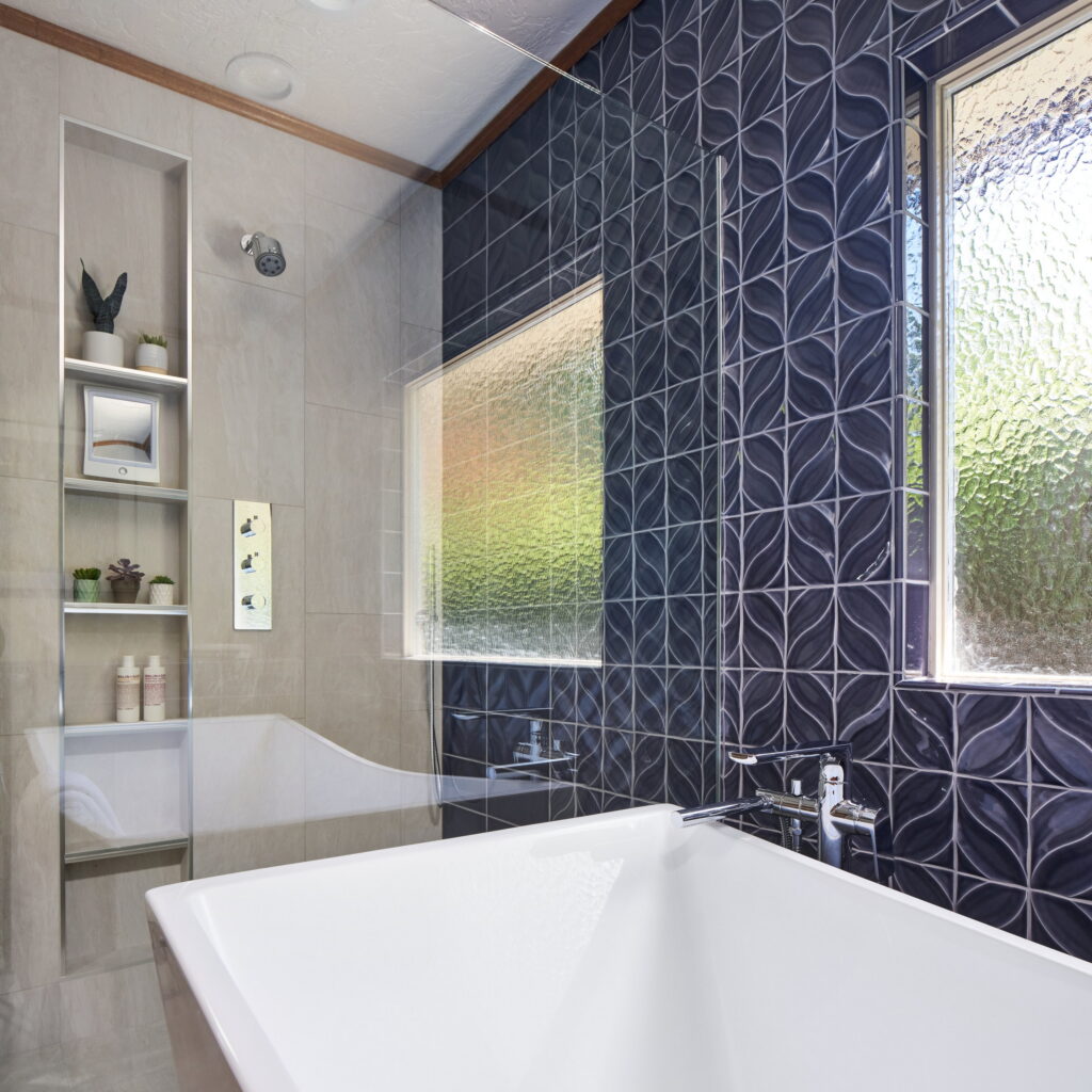 Freestanding tub against the patterned navy tile, with the shower niche visible beyond the glass.