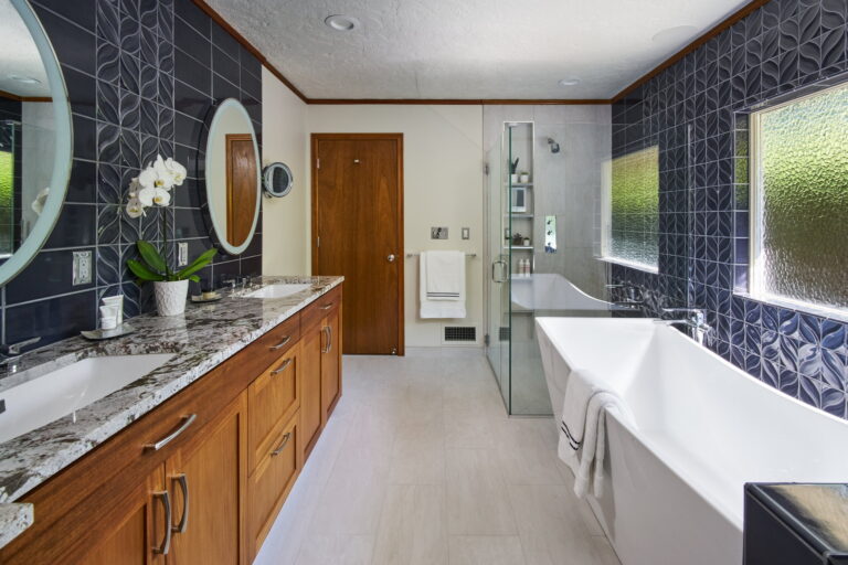 Remodeled Sellwood primary bathroom with a deep navy patterned tile wall, freestanding tub, and a mahogany double vanity.