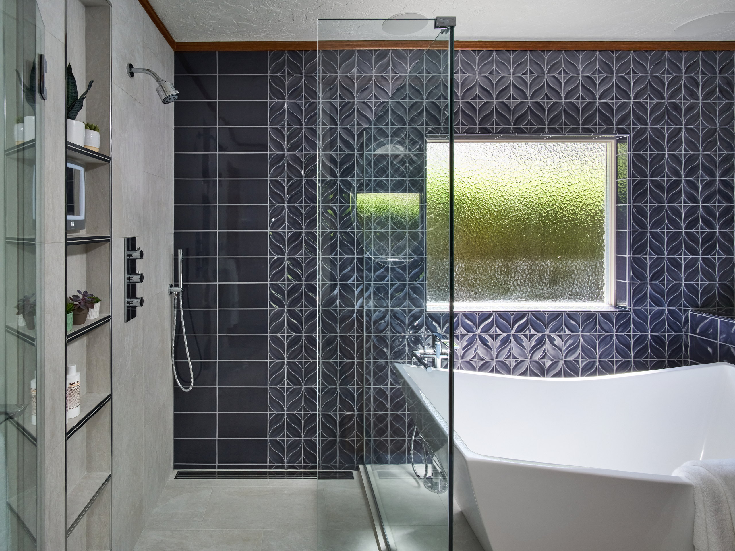 Walk-in shower with a linear drain and recessed niche, opening to the tub beneath an obscured-glass window.