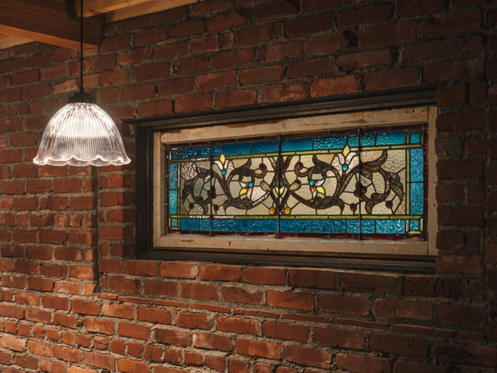 Salvaged stained-glass window with a scrolling floral pattern set into the basement brick wall.